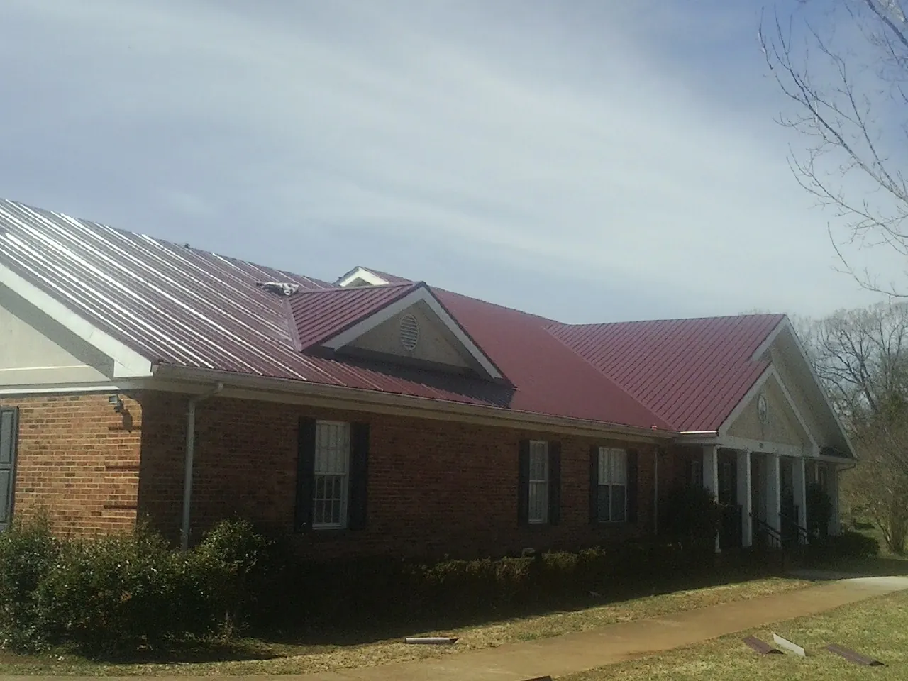 Red metal roof with gabled entries on a long brick building, from a Hail Damage Roof Repair job in West Shokan