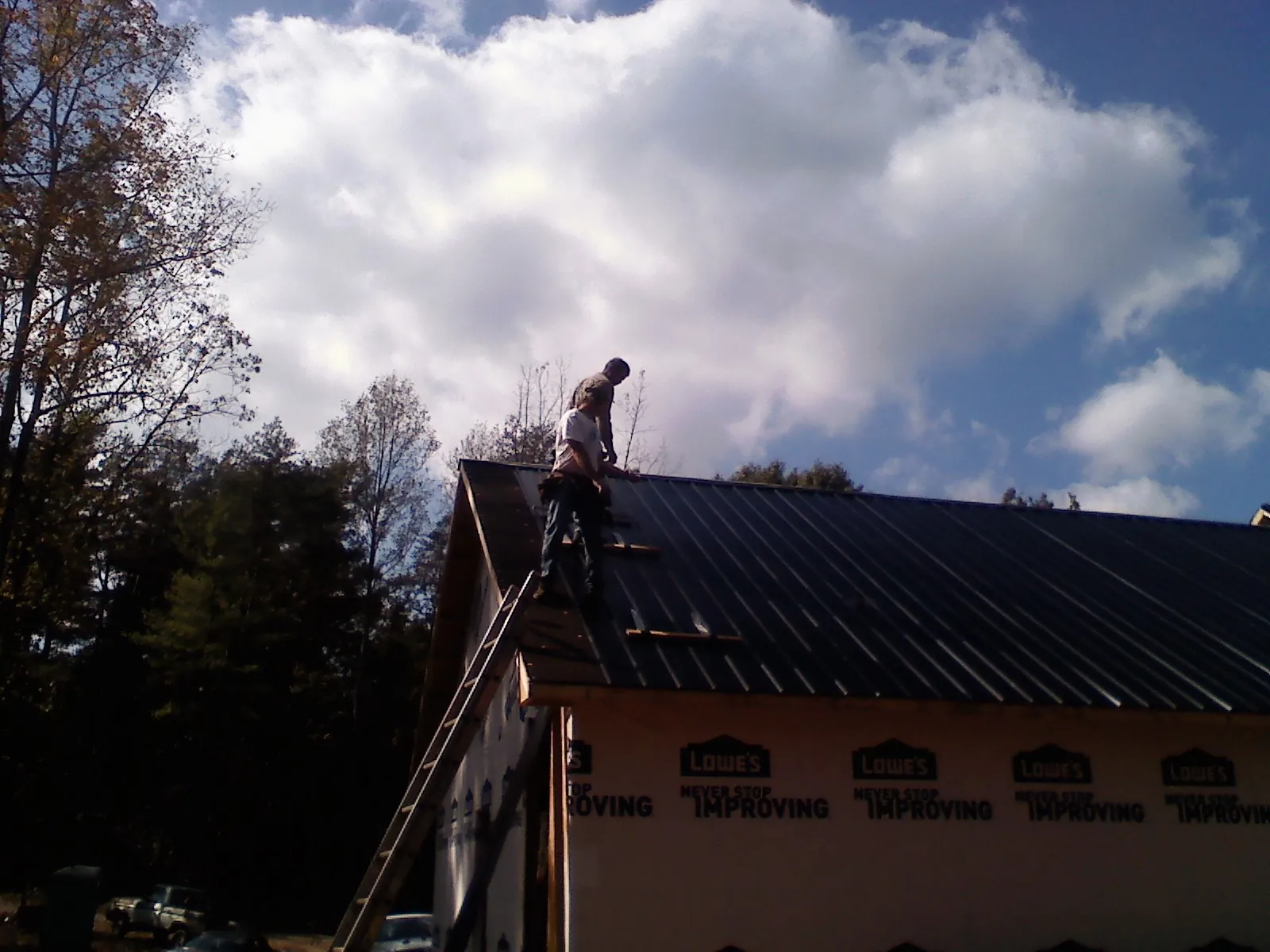 Roofer fastening dark metal panels high against a cloudy sky, from a Roof Inspection job in West Shokan