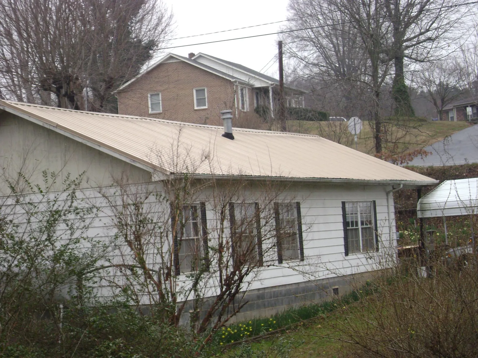 Tan metal roof on a white sided house set into a hillside — Commercial Roofing by Roofing Brothers in West Shokan